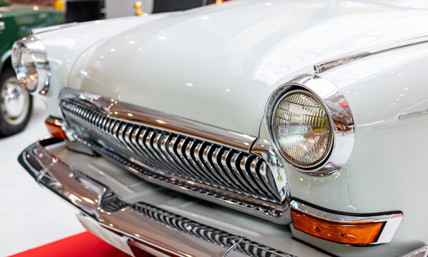 Close-up of the round headlamps of a white classic car. Beautifully restored chrome details of a historic vehicle. Round headlight of a white old timer car