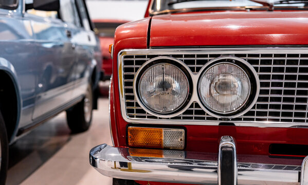 Close-up of the round headlights of a red classic car. Beautifully restored chrome parts of a historic vehicle. Round headlight of a red vintage car.