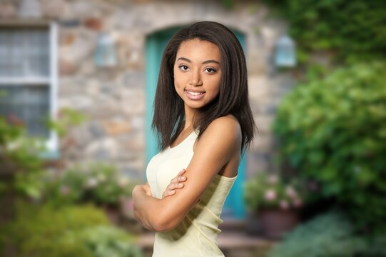 Smiling young Black woman standing with arms crossed outside a stone house