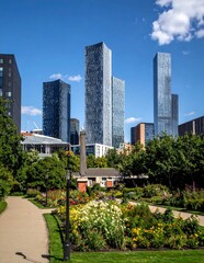 Fototapeta premium Modern Glass Skyscrapers Rising Above Lush Flower Garden in Sunny Urban Park