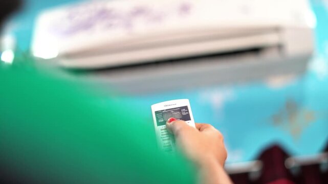 Close Up of Hand Using Remote Control to Turn On Wall Air Conditioner Unit. Adjusting Room Temperature with Remote Control for Split System AC in Summer. 