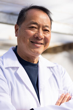 Senior Chinese man standing arms crossed, smiling, wearing white lab coat and dark crewneck in lab