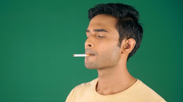  A young Indian man lighting a cigarette while standing sideways. Green screen / Chroma shoot. An attractive male inhaling and exhaling vape while smoking - addiction  addict  lifestyle  bad habits