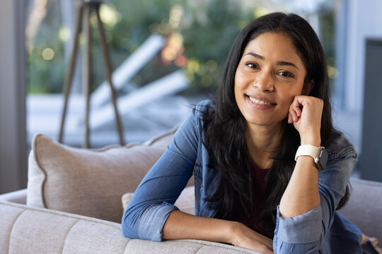 African American woman sitting on sofa near glass window, wearing denim jacket, white smartwatch