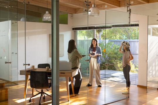 Diverse female coworkers demoing VR in glass office holding headset box and controller near desk