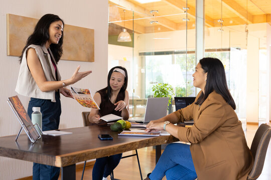 Diverse female team presenting food brochure and reviewing notes in office with laptop, copy space