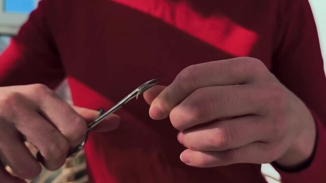 Hands trim a fingernail with metal clippers in close up. The nail cutting motion continues in indoor light. Personal grooming, hygiene, and self care use..