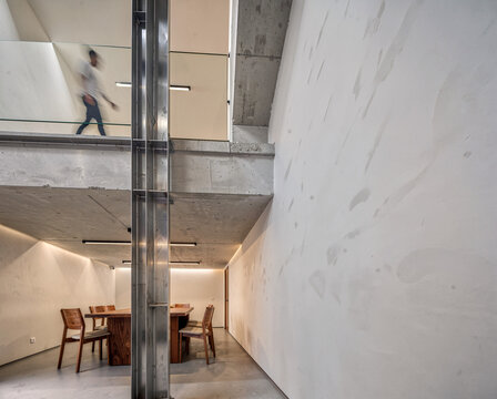 Modern minimalist interior with dining table, concrete walls, and person walking on upper level