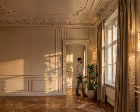 Man walking through elegant room with ornate ceiling and warm sunlight streaming in