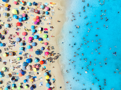 Aerial view of colorful umbrellas on sandy beach, swimming people in blue sea on sunny summer day. Mallorca, Balearic Islands, Spain. Turquoise water. Travel and vacation. Top down view. Tropical