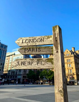 Weathered Wooden Direction Sign Pointing to London Paris and New York in Urban Square