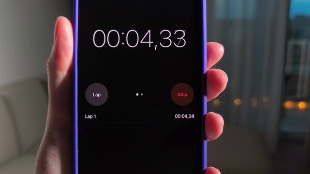 Hand holds smartphone with running stopwatch app. The timer advances through lap tracking on a dark screen. Mobile time management and workout timing concept..