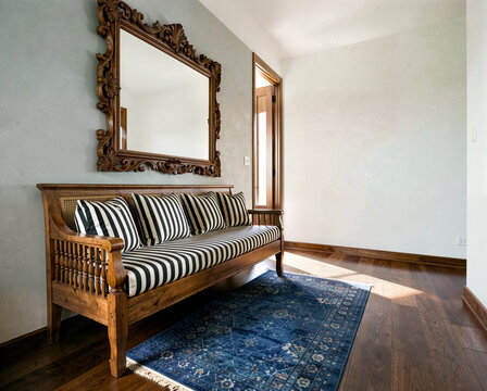 Elegant wooden bench with striped cushions under ornate mirror in sunlit hallway