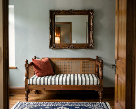 Vintage wooden bench with striped cushion under ornate mirror in cozy room interior