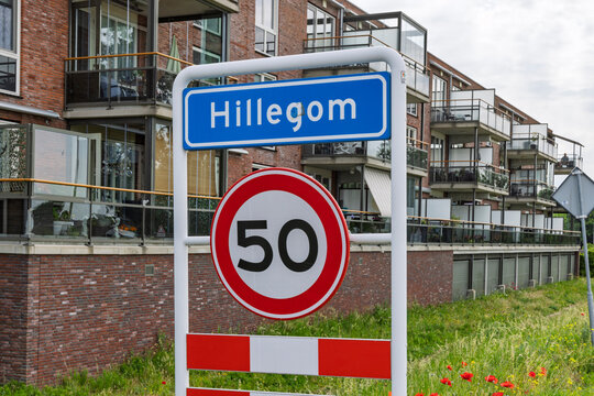 Hillegom, Netherlands - Blue city name sign for Hillegom combined with a 50 kilometers per hour speed limit sign in front of apartment buildings.