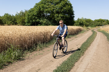 Fototapeta premium Young man cycling next to wheat field