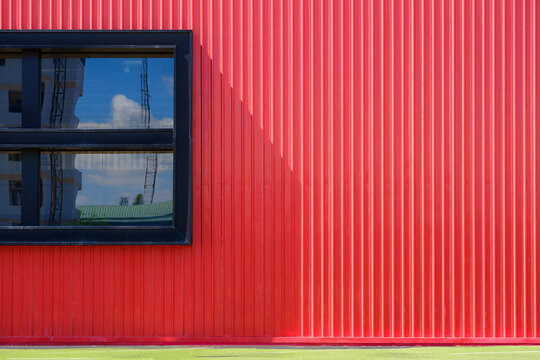 Glass window on red corrugated steel modern building wall with artificial turf on the floor, exterior geometric architecture background in minimal design 