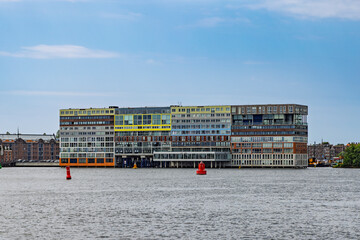 Obraz premium Amsterdam, Netherlands - The iconic and colorful Silodam apartment building standing directly in the water of the IJ river under a clear blue sky.