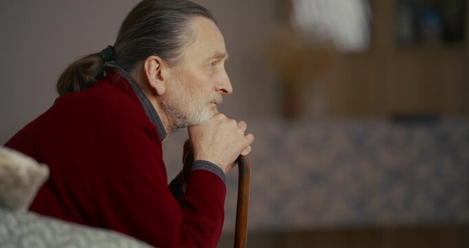 Adult in red sweater holding cane beside sofa cushion in living room