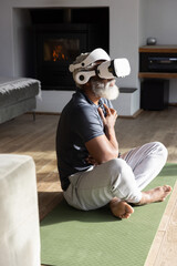 Obraz premium Senior African American man sitting cross-legged on green yoga mat at home wearing white VR headset