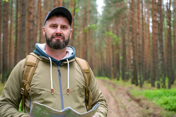 Bearded man stands on forest road and checks paper map for orientation and route finding. Outdoor navigation, hiking planning and travel concept © Dmitrii Masquerade