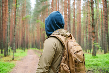 man with backpack stands on forest road and looks ahead into pine woodland. Hiking, route choice and quiet travel concept © Dmitrii Masquerade