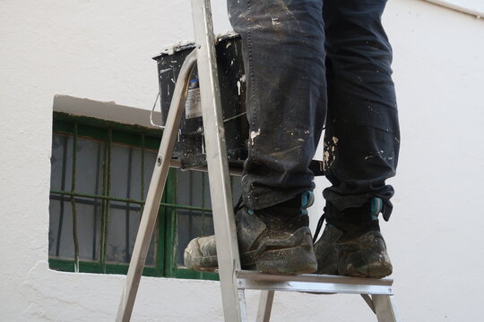 Un pintor est&aacute; en la escalera pintando la pared.