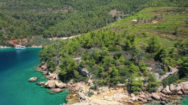 Aerial view of tourist excursion boat anchored in secluded turquoise bay surrounded by dense pine forests in Gulf of Gokova, Marmaris, Turkey