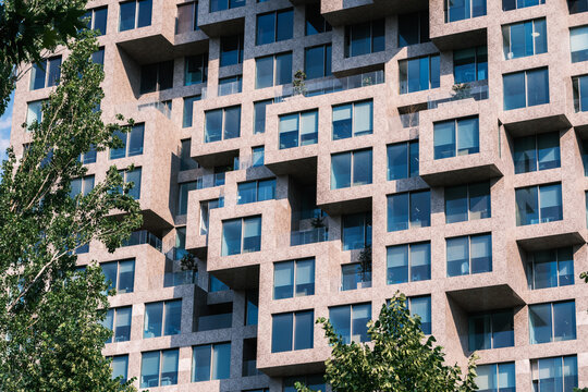 View of the modern pixelated facade of a contemporary building with staggered windows and balconies behind green trees in Tirane, Tirana County, Albania.