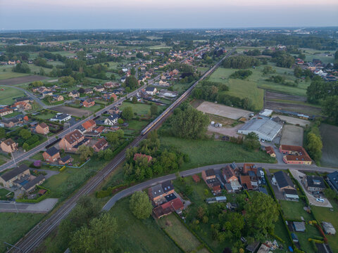 Diepenbeek, Belgium. Aerial drone view of suburban village with railway corridor, residential housing and agricultural landscape at sunrise