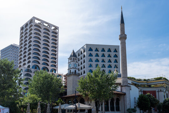 View of the historic Et'hem Bey Mosque and Clock Tower standing alongside modern architectural high-rises under a clear blue sky in Tirana, Tirana County, Albania.