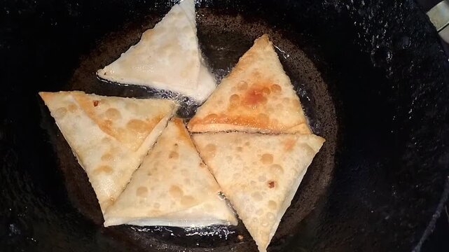 Golden brown samosas frying in hot oil inside a deep frying pan triangle shaped savory pastries in a metal filled with oil, capturing