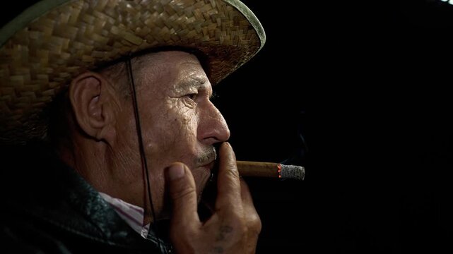 Low-key portrait of an elderly farmer partially illuminated at night while smoking a cigar. Thick smoke, deep shadows, and focused lighting create a dramatic and visually compelling character study.