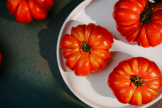 Ripe red heirloom tomatoes with water drops on white plate and dark green background