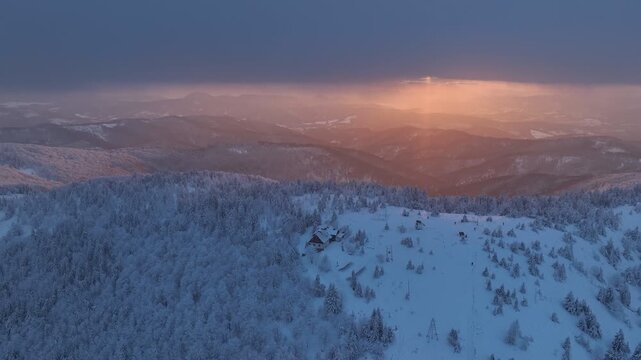 Drone orbital flight of mountain summit and chalet against colorful sunset horizon in winter