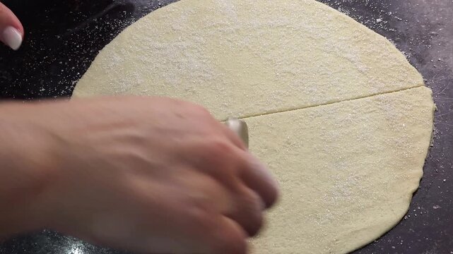 Top view close up of hands cutting a round rolled shortcrust pastry dough sprinkled with sugar into triangles using a pizza wheel roller cutter. Process of preparing homemade sweet crescent rolls or r
