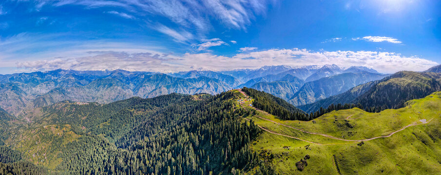 Aerial view of the lush green Siri Paye meadows and Shogran ridge with dense pine forests and distant snow-capped peaks in Balakot, Khyber Pakhtunkhwa, Pakistan.