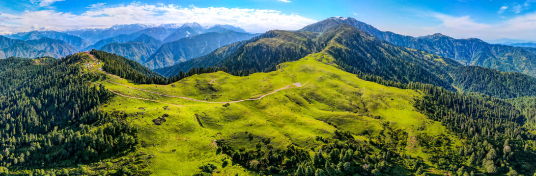 Aerial view of the lush green Siri Paye Meadows and winding mountain tracks surrounded by dense pine forests and distant snow-capped peaks in Balakot, Khyber Pakhtunkhwa, Pakistan.