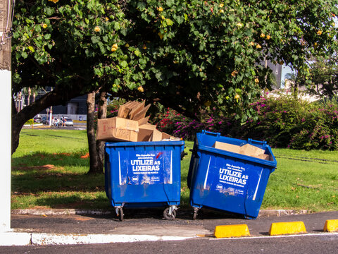 Marilia, SP, Brazil. April 16, 2026. Two blue plastic waste containers filled with cardboard boxes for recycling, located in a public park area in downtown Mar&iacute;lia, Sao Paulo state. 