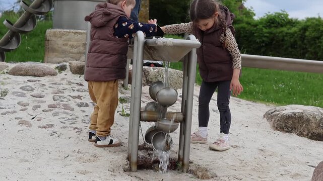 Father with two little kids playing with water pump and Archimedes screw at outdoor playground