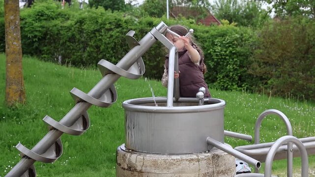 Father with two little kids playing with water pump and Archimedes screw at outdoor playground