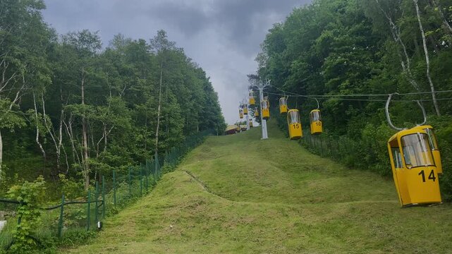 Aerial ropeway transport system with hanging gondolas moving over a grassy hill. Summer outdoor recreation and tourism.