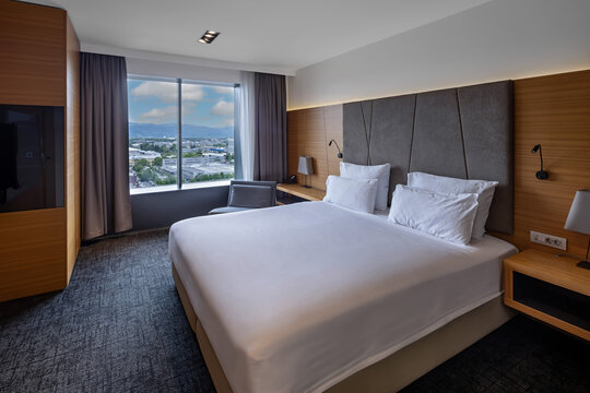 Modern luxury hotel room with king size bed elegant wooden panels and panoramic city view window