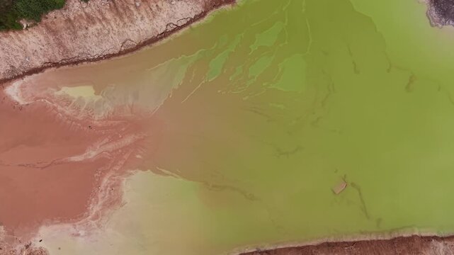 Overhead view of contaminated settling pond with vivid orange-brown and yellow-green discoloration caused by acid mine drainage at an open pit quarry, highlighting severe environmental pollution