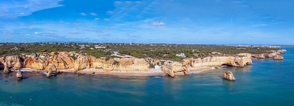 Aerial view of Marinha Beach featuring golden limestone cliffs and turquoise waters under a clear blue sky in Lagoa, Faro District, Portugal.
