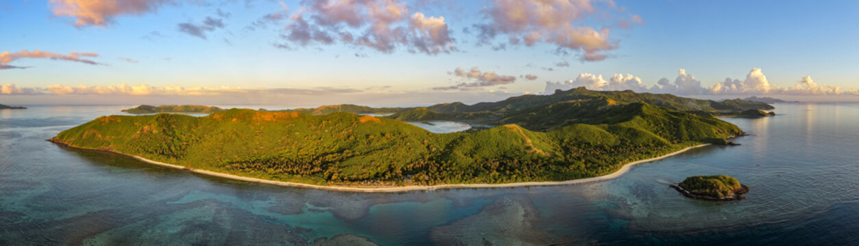 Aerial view of Naviti Island with lush green hills, white sandy beaches, and vibrant turquoise coral reefs under a soft sunset sky Naviti, Western Division, Fiji.