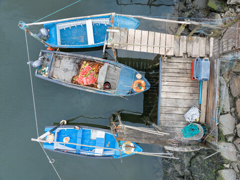 Aerial view of three blue fishing boats moored at a rustic wooden pier with fishing nets and equipment in Aveiro, Aveiro District, Portugal.