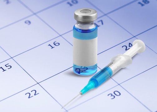 Vaccine vial and medical syringe lying on a calendar for healthcare schedule planning