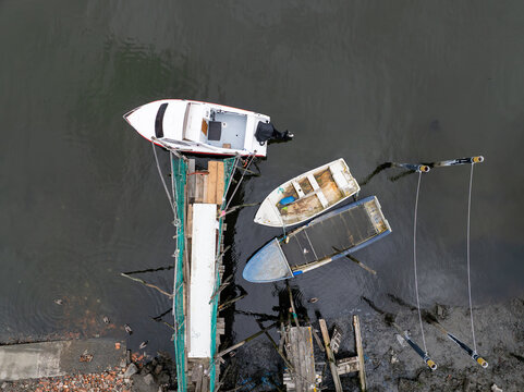 Aerial view of small boats moored at a rustic wooden pier over dark water with a muddy shoreline Aveiro, Aveiro District, Portugal.