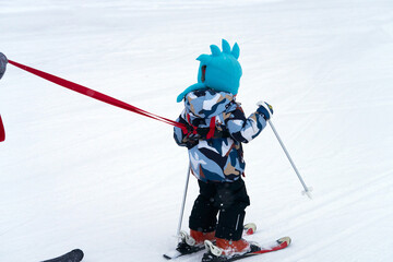 Naklejka premium Teaching little ones to ski. A small child, wearing a harness, descends a snowy slope.